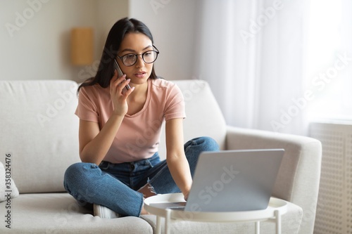 Girl Working On Laptop Talking On Mobile Phone Sitting Indoors