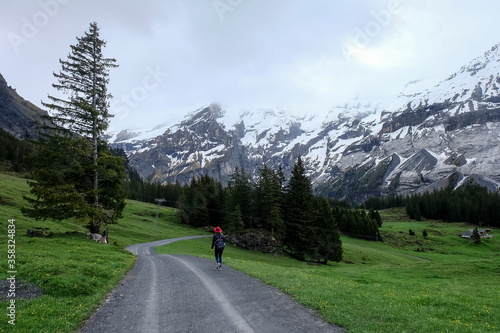 A woman trekking along asphalt road in valley. Snow capped mountain in background.