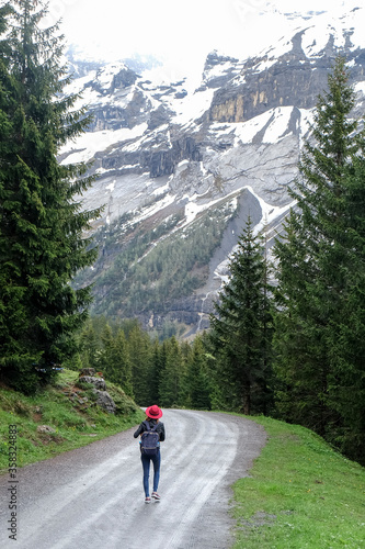 A woman trekking along asphalt road in valley. Snow capped mountain in background.