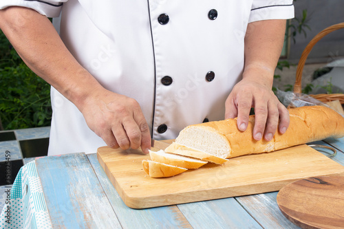 Chef holding knife cutting slide bread making on wooden board