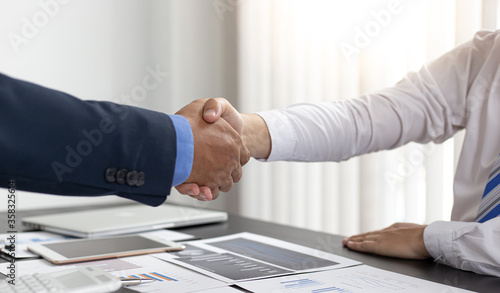 Both businessmen shake hands to congratulate the office of the meeting.