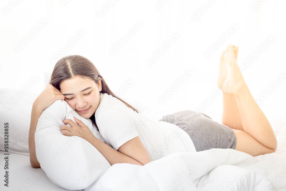 Portrait of young lovely and beautiful woman is lying down and smiling happily on the white bed, white pillows, white blankets and white bedroom with warm weather and mild sunshine in the morning. Portrait of young lovely and beautiful woman is lying down and smiling happily on the white bed, white pillows, white blankets and white bedroom with warm weather and mild sunshine in the morning.
