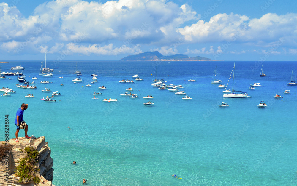 paradise clear torquoise blue water with boats and cloudy blue sky in background in Favignana island, Cala Rossa Beach, Sicily South Italy. paradise clear torquoise blue water with boats and cloudy blue sky in background in Favignana island, Cala Rossa Beach, Sicily South Italy.