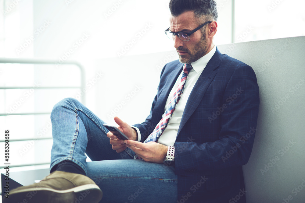 Confident male director f company dressed in trendy formal outfit and glasses using application on smartphone for banking online, thoughtful businessman reading financial news using wifi connection Confident male director f company dressed in trendy formal outfit and glasses using application on smartphone for banking online, thoughtful businessman reading financial news using wifi connection