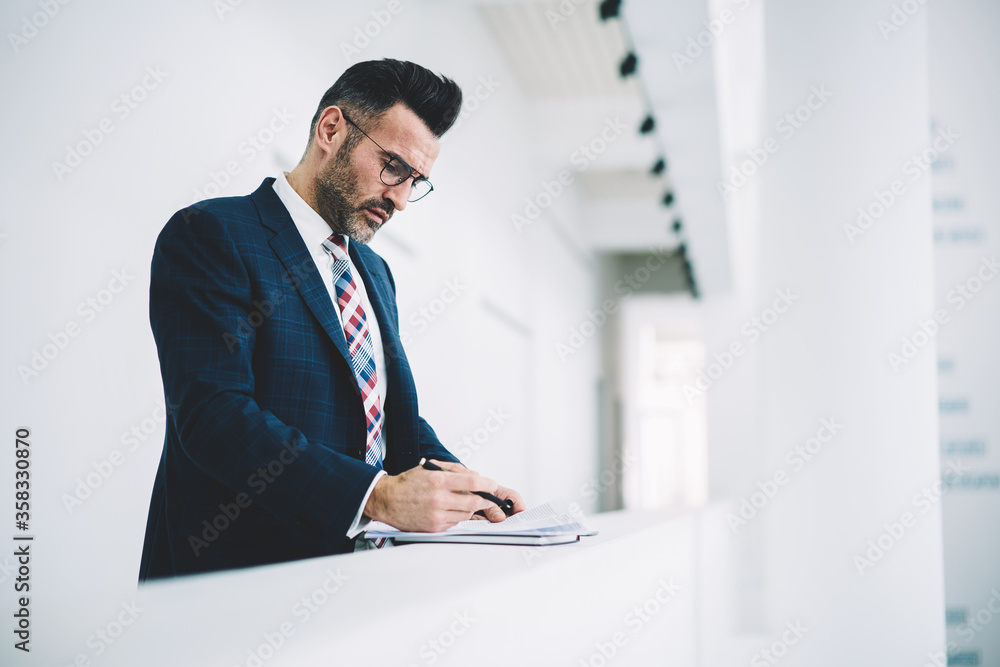 Pensive mature entrepreneur dressed in formal wear checking financial documents working in office interior.Confident proud ceo middle aged reading information and signing accounting reports Pensive mature entrepreneur dressed in formal wear checking financial documents working in office interior.Confident proud ceo middle aged reading information and signing accounting reports