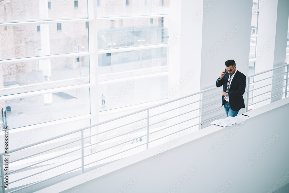 Obraz premium Top view of busy mature businessman talking on smartphone while looking at watch to checking time hurrying on meeting in office.Middle aged entrepreneur in formal wear calling on cellular device