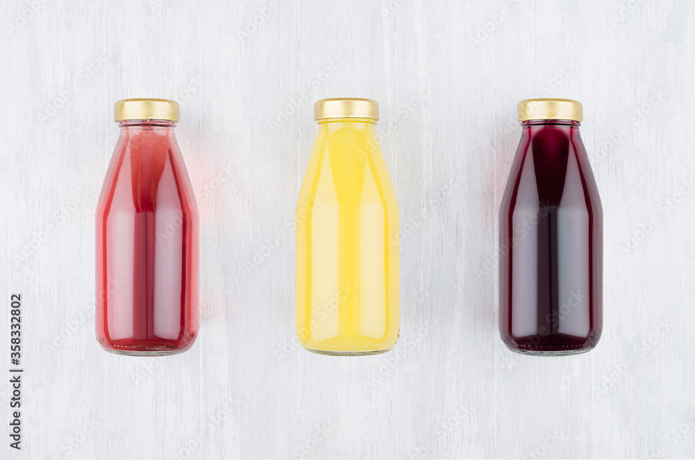 Set of organic fruits juices - orange juice, strawberry, currant in glass bottles  on white wood background, mock up for design, advertising, branding product.