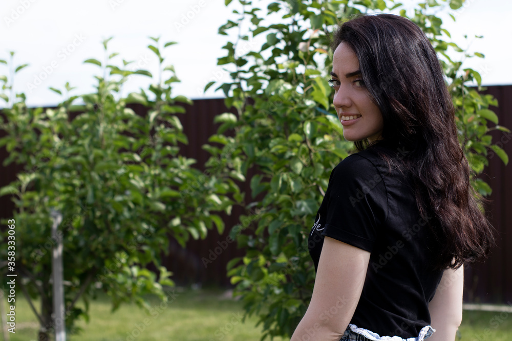 Charming young brunette woman in a black T-shirt and denim shorts. In the country, in the garden. High quality photo Charming young brunette woman in a black T-shirt and denim shorts. In the country, in the garden. High quality photo