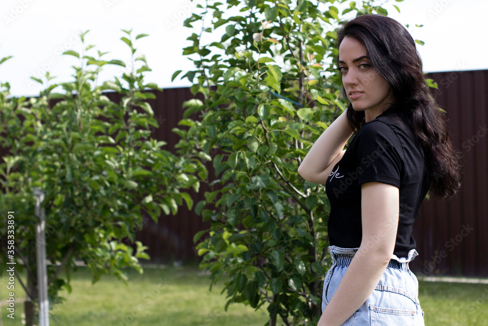 Charming young brunette woman in a black T-shirt and denim shorts. In the country, in the garden. High quality photo