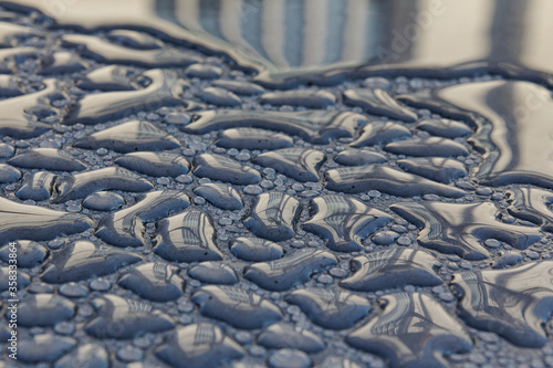 A building facade is reflected in early morning dew drops.