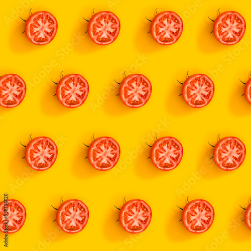 Diagonal pattern from ripe juicy tomatoes cut in half on bright yellow background. Creative minimalist flat lay. Vitamins vegan healthy diet concept