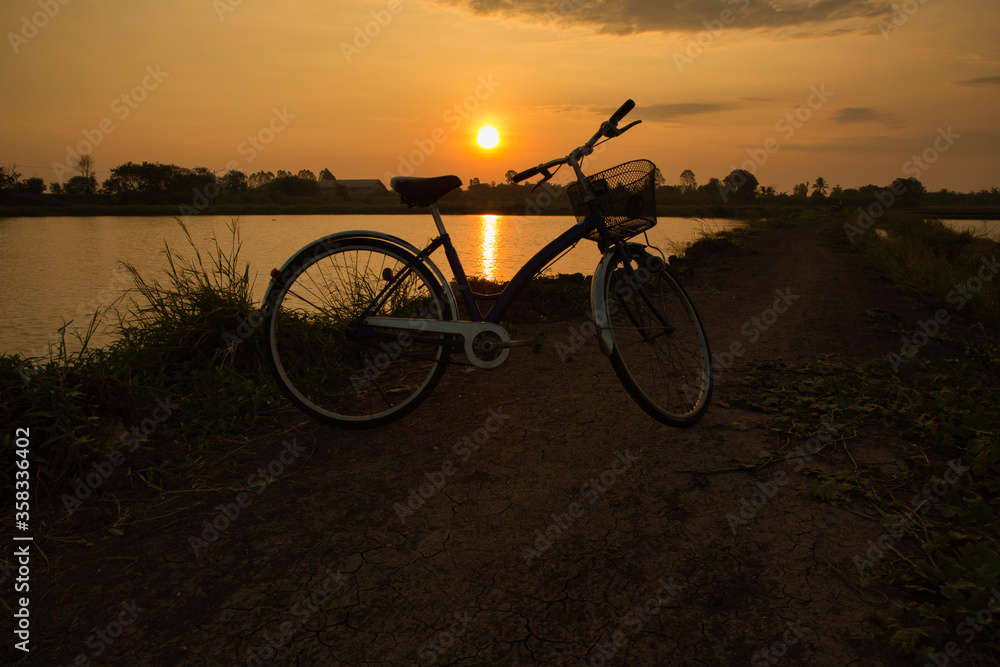 The bicycle parking in the field with the background of sunrise. This is art of silhouette and relaxing concept.