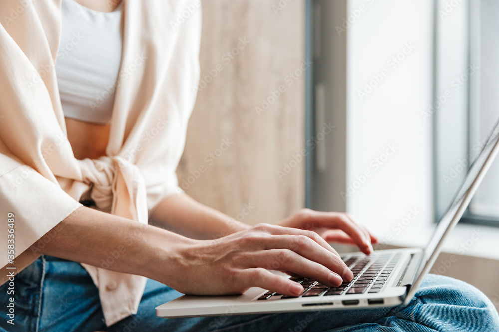 Naklejka premium Cropped image of woman working with laptop while sitting on floor
