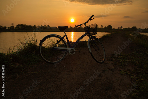 Fototapeta Naklejka Na Ścianę i Meble -  The bicycle parking in the field with the background of sunrise. This is art of silhouette and relaxing concept.