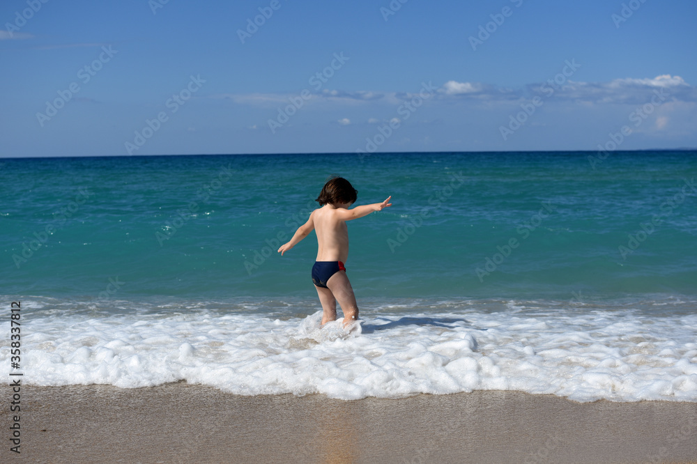 Little boy enjoying on beach. Child sit on beach and play in sea on summer vacation Little boy enjoying on beach. Child sit on beach and play in sea on summer vacation