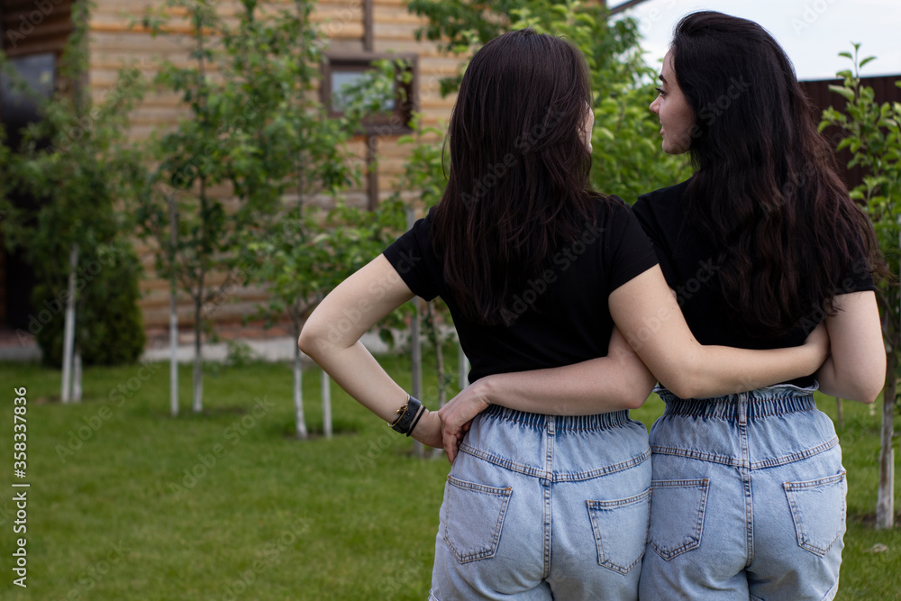 Fototapeta premium Two young brunette women in a black T-shirt and denim shorts hugging. Sisters, girlfriends. family and friendship concept. High quality photo