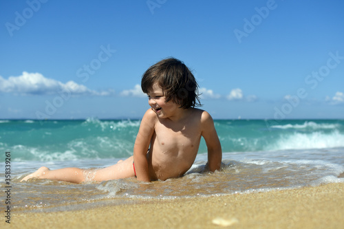 Little boy enjoying on beach. Child sit on beach and play in sea on summer vacation © Ivan