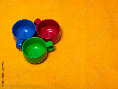 Three plastic mugs in RGB colors on a yellow fabric background