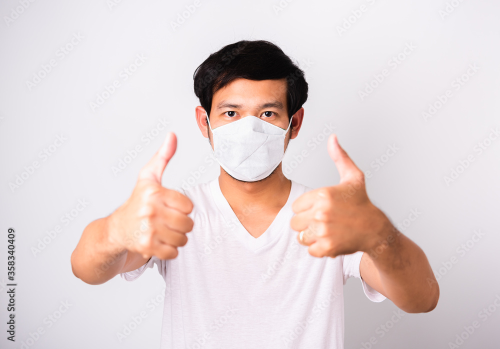 Asian handsome Man wearing surgical hygienic protective cloth face mask against coronavirus he show finger thumb for good, studio shot isolated white background, COVID-19 medical concept Asian handsome Man wearing surgical hygienic protective cloth face mask against coronavirus he show finger thumb for good, studio shot isolated white background, COVID-19 medical concept