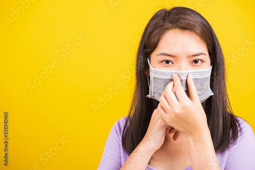 Closeup of portrait Asian young teen woman wearing face mask protective against coronavirus or COVID-19 virus showing demonstrating correct step, studio shot isolated yellow background