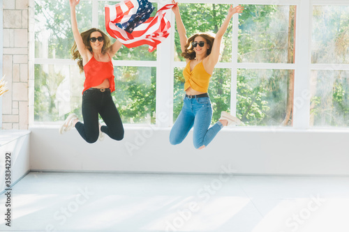 Fototapeta Naklejka Na Ścianę i Meble -  Two attractive young girls in sunglasses with the American flag, U.S.A independence day celebrations