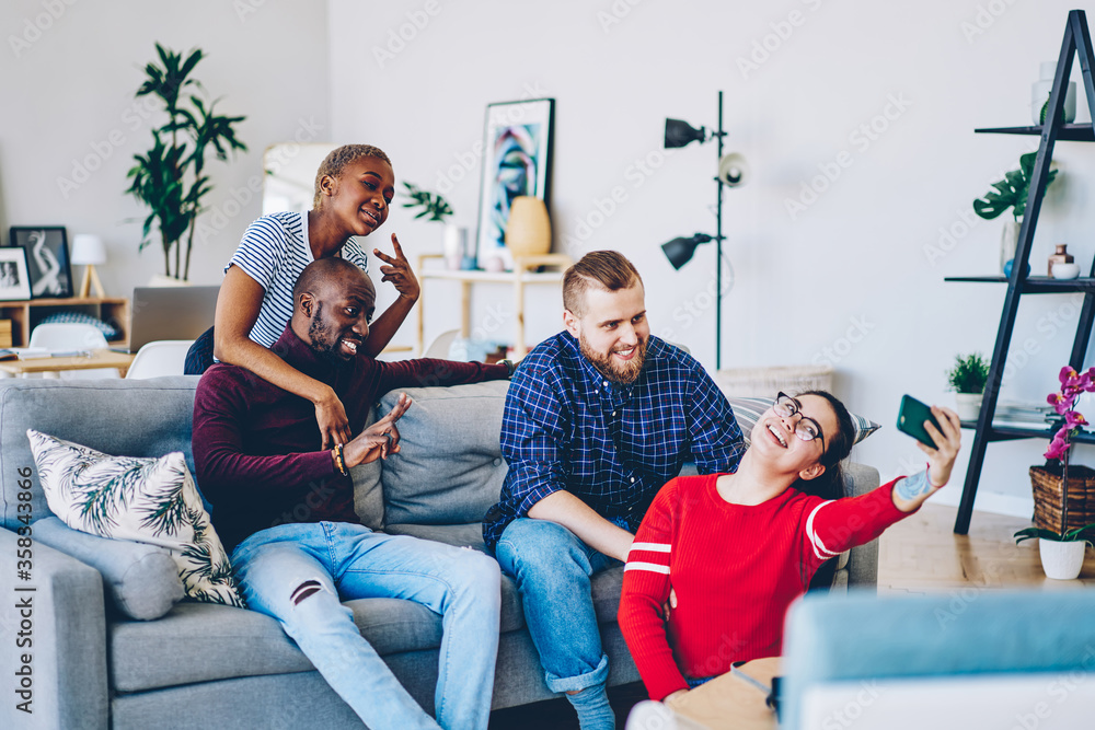 Positive multiracial friends having fun at apartment posing for selfie on smartphone camera, young cheerful male and female hipsters taking photo on mobile phone during meeting at home interior. Positive multiracial friends having fun at apartment posing for selfie on smartphone camera, young cheerful male and female hipsters taking photo on mobile phone during meeting at home interior.