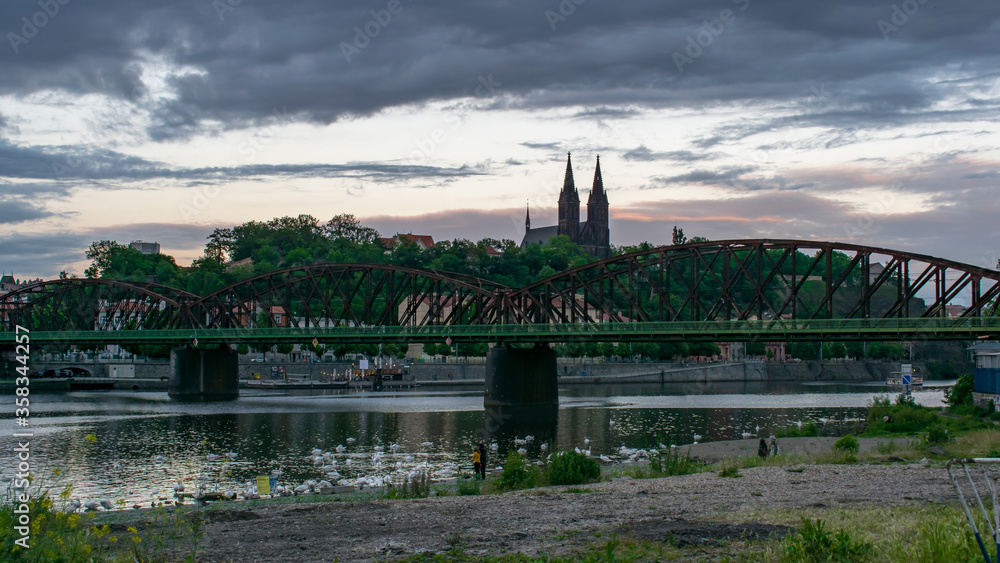 A panorama of the Vltava river banks with the Railway bridge, and Basilica of St. Peter and St. Paul at Vysehrad in the background 