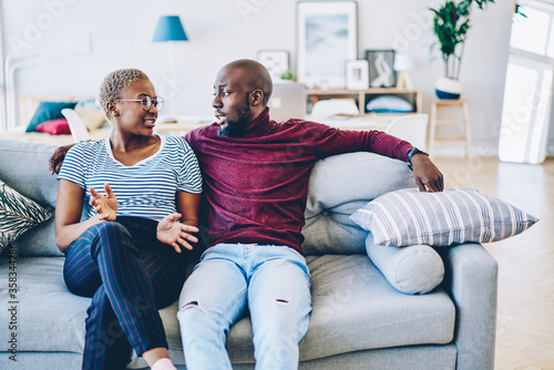 Young african american marriage having discussion about problem sitting at couch in living room, romantic couple talking about relationship looking at each other spending time together photo