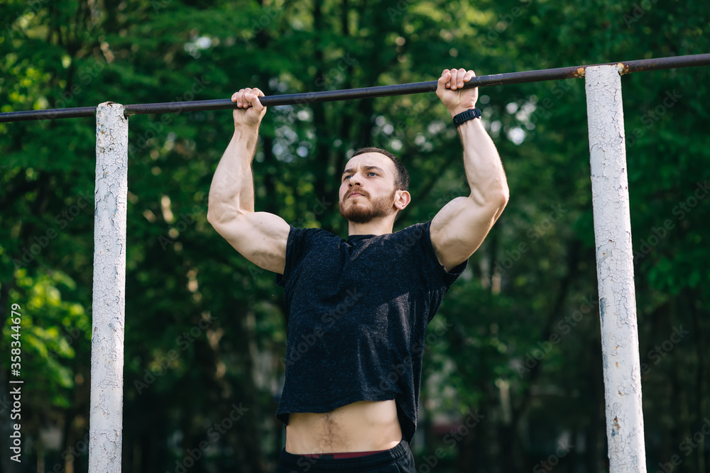 strong athlete doing pull-up on horizontal bar in park. Man Doin strong athlete doing pull-up on horizontal bar in park. Man Doin