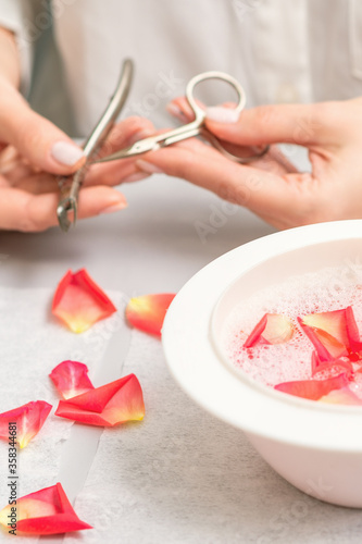 Pink petals in bowl with pure water on white table in beauty spa manicure salon.