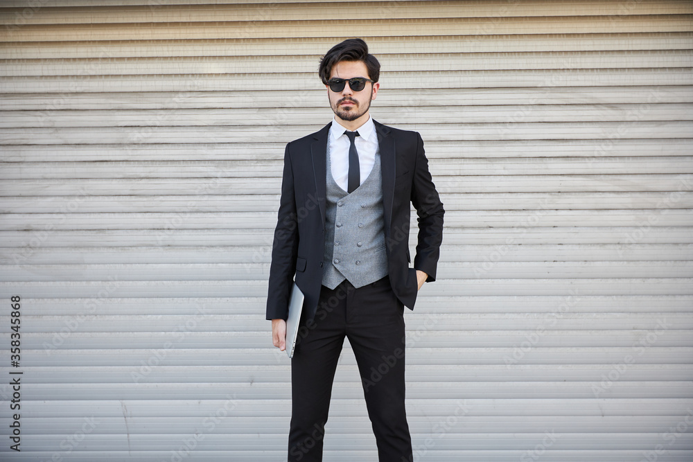 Portrait of a young businessman in a suit outdoor holding a laptop Portrait of a young businessman in a suit outdoor holding a laptop