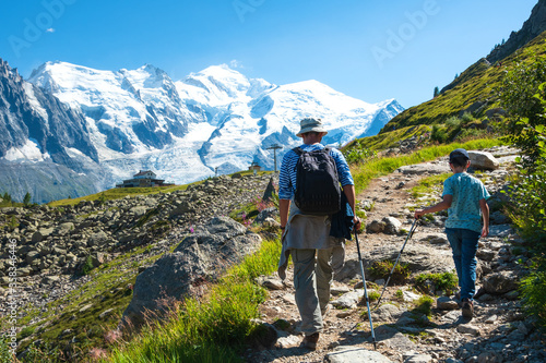 Father and son hiking in French Alps in summer. Back view. Snow covered Mont Blanc mountain and Plan Praz cable car station at background. Active holidays at nature concept. 