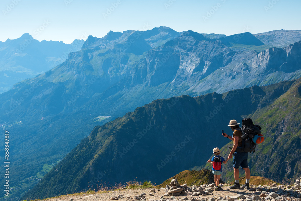 Family summer holidays in mountains. Father and his little son admire and take photo of  Alps mountain landscape. Back view. Active vacation with kid, fathers day concepts. France tourism background.