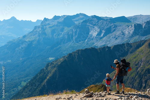 Family summer holidays in mountains. Father and his little son admire and take photo of Alps mountain landscape. Back view. Active vacation with kid, fathers day concepts. France tourism background.