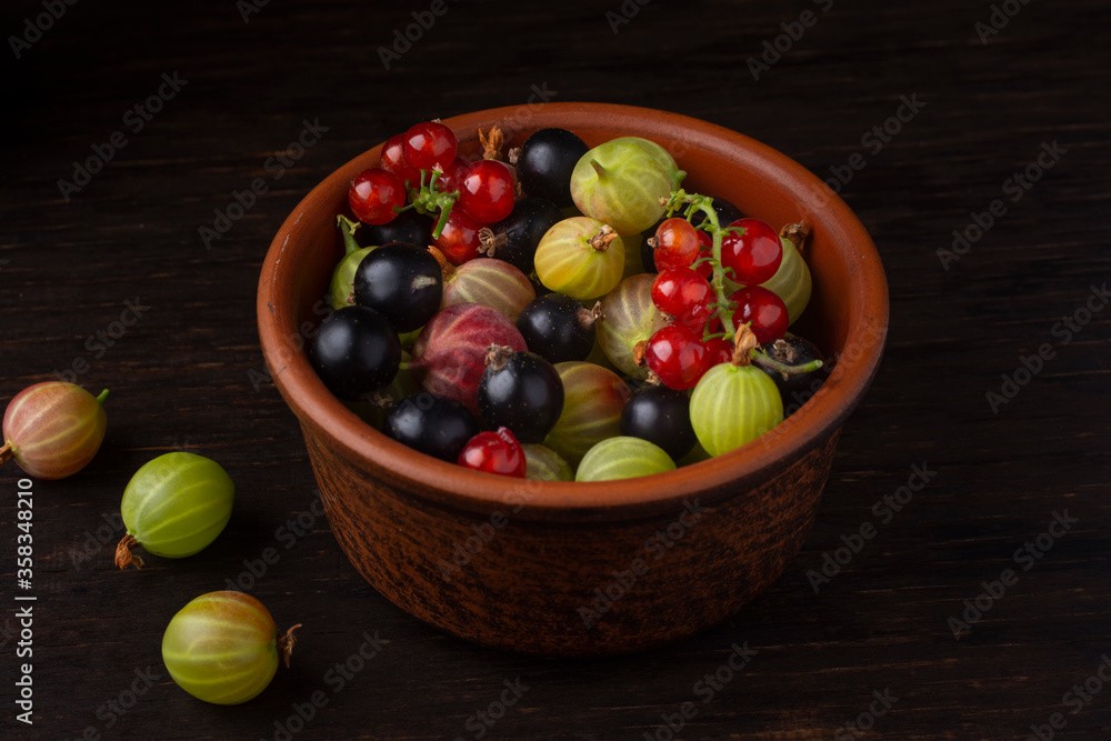 Berries of currant and gooseberry in a ceramic bowl on a dark background. Berries of currant and gooseberry in a ceramic bowl on a dark background.