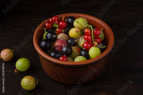 Fototapeta Naklejka Na Ścianę i Meble -  Berries of currant and gooseberry in a ceramic bowl on a dark background.
