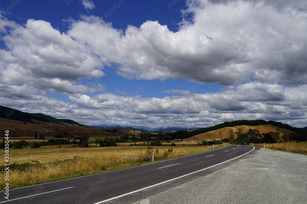 Typical New Zealand road on South Island with blue sky and clouds.