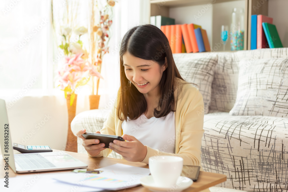 Asian girl playing online games application or chatting text message with friend by using smart phone smiley face at house during break time of working at home that make her get relax, fun, happy Asian girl playing online games application or chatting text message with friend by using smart phone smiley face at house during break time of working at home that make her get relax, fun, happy