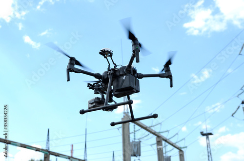 Fototapeta Naklejka Na Ścianę i Meble -  Pro quadcopter with camera aboard flying in a sky, electric pylon, cables and insulators on the background
