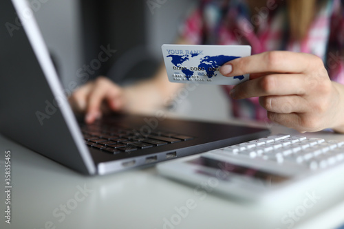 Close-up of person holding white plastic credit card and typing on modern laptop. Remote payment for service. Female customer order clothing. Online shopping and technology concept