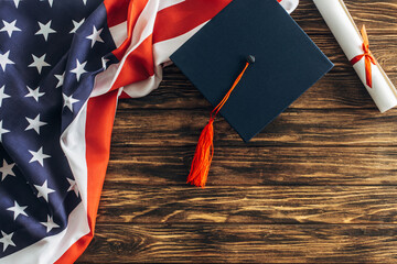 top view of diploma and graduation cap near american flag with stars and stripes on wooden surface