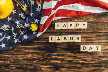 top view of safety helmet and instruments near happy labor day lettering near american flag on wooden surface