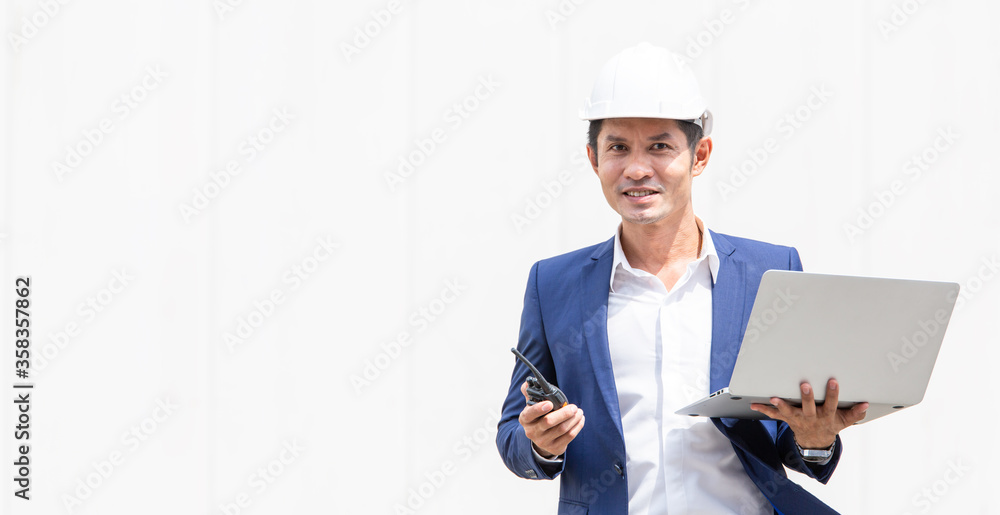 Portrait of Asian engineer foreman holding laptop and walkie talkie for on white wall background of container box. manager smile confident in positive mood. Construction business concept, copy space Portrait of Asian engineer foreman holding laptop and walkie talkie for on white wall background of container box. manager smile confident in positive mood. Construction business concept, copy space