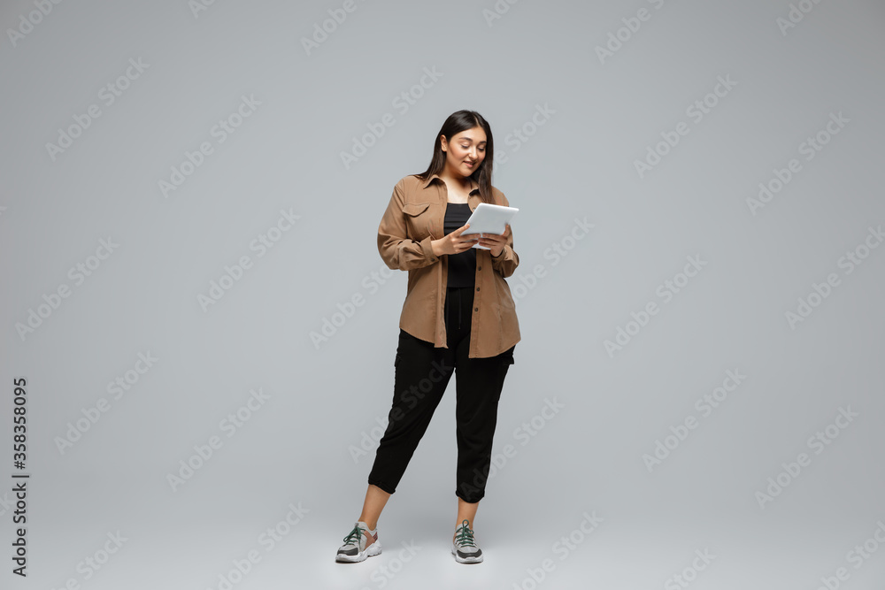 Fashionable, stylish. Young woman in casual wear on gray background. Bodypositive character, feminism, loving herself, beauty concept. Plus size businesswoman scrolling tablet. Inclusion, diversity. Fashionable, stylish. Young woman in casual wear on gray background. Bodypositive character, feminism, loving herself, beauty concept. Plus size businesswoman scrolling tablet. Inclusion, diversity.