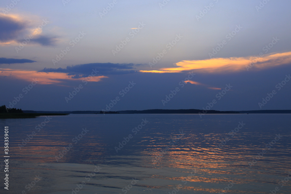 Sunset behind the blue clouds above the quiet lake water