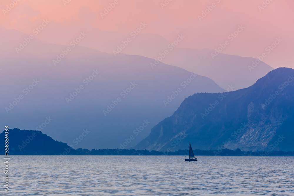 Pink dawn on lake Maggiore, Italy. A small sailing yacht against the background of the Alpine mountains and the dawn sky. Fog over the mountains.