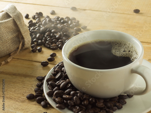 Roasted coffee beans with a cup of smoke on a wooden background.