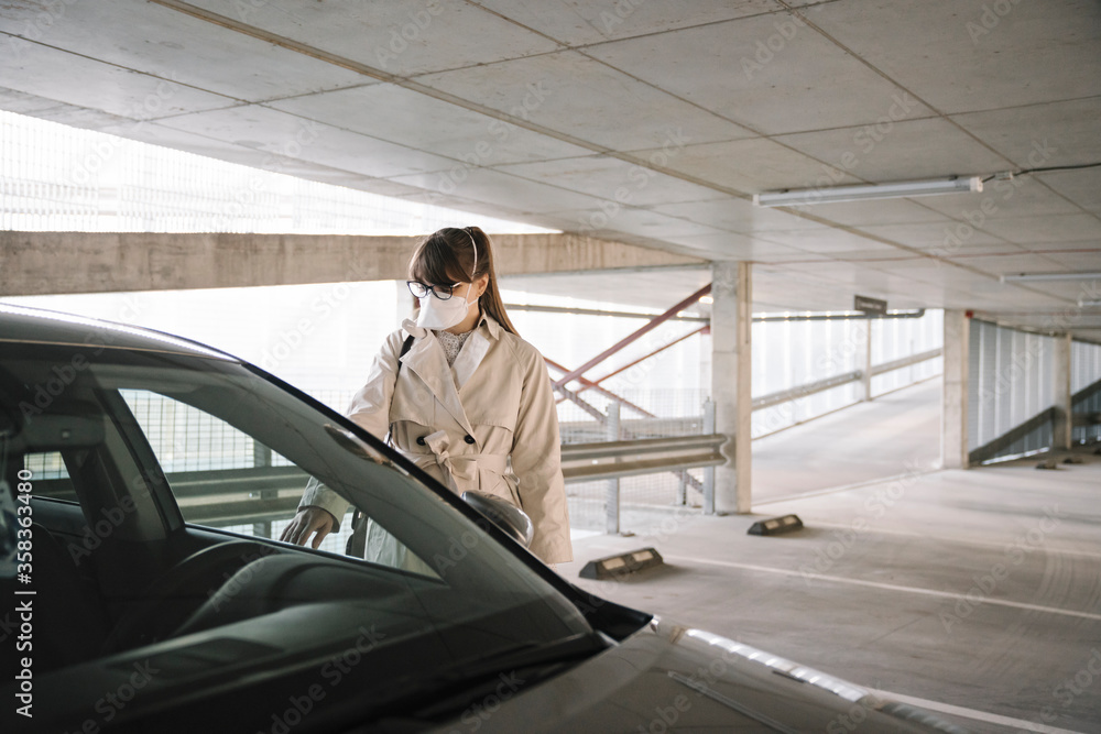 Woman wearing face mask opening car in a car park Woman wearing face mask opening car in a car park
