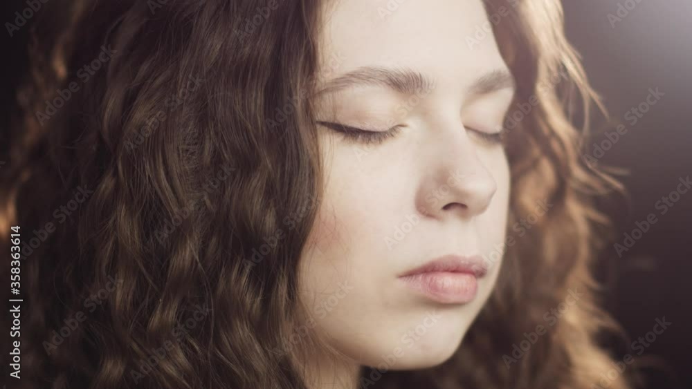 Close-up portrait of a young curly relaxing woman closing her eyes and taking deep breath. Girl snapps yoga in the studio Close-up portrait of a young curly relaxing woman closing her eyes and taking deep breath. Girl snapps yoga in the studio
