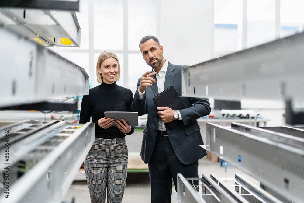 Businessman and woman with tablet at metal rods in factory hall Businessman and woman with tablet at metal rods in factory hall